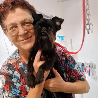 אירינה מחזיקה כלב גריפון שחור על שולחן המספרה